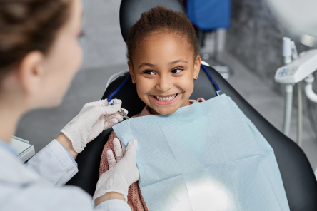 A female child in a dental child while a female dentist conducts a dentist appointment.