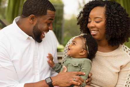 A father and mother holding a baby while smiling.